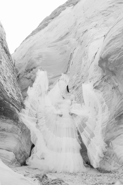 Bridal portrait of a bride in ruffled gown with a layered tulle skirt and sheer sleeves, standing among sandstone canyon rock formations