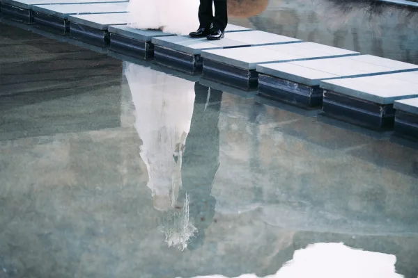 Couple portrait with wedding reflection photo in a reflecting pool, bride’s veil and dress hem beside groom suit and dress shoes on stone steps