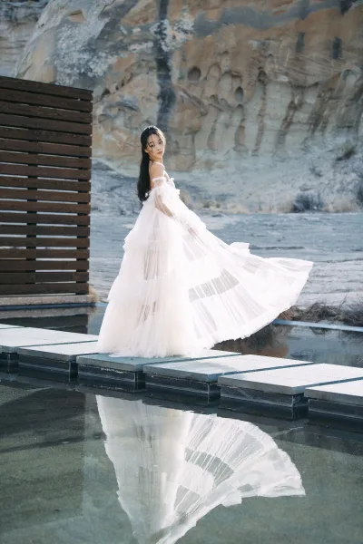 Bridal portrait of a bride in an off the shoulder wedding dress with a tulle skirt, standing by a reflecting pool with rock cliffs and stepping stones