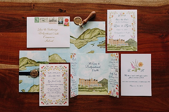 Invitation suite with watercolor wedding invitation, save the date, RSVP and details cards, envelope, postage stamps, and wax seal on wood tabletop