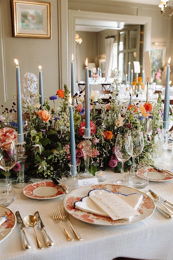 Reception tablescape with a wedding table centerpiece of wildflowers, taper candles, patterned china, and place cards in an elegant dining room with chandelier