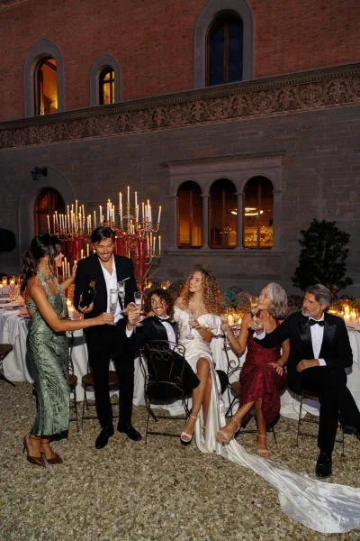 Wedding toast with clinking champagne glasses at the table, candelabras aglow in a historic stone courtyard.