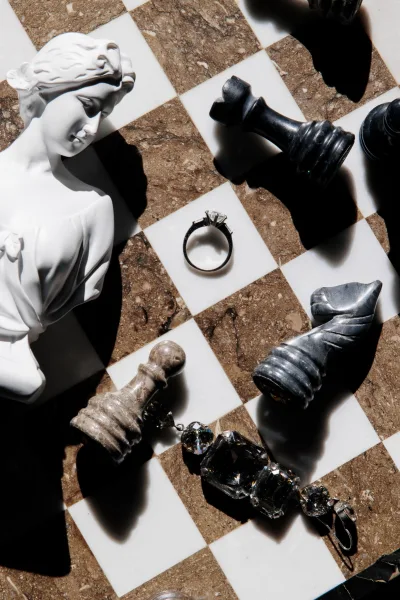Engagement ring, a solitaire diamond ring, styled with chess pieces on a marble checkerboard tile, captured in a graphic flat lay.