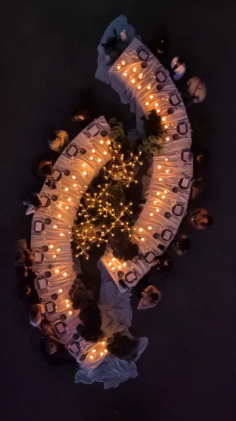 Reception tablescape set as a candlelit dinner table, with soft fairy lights, on dark pavement at an outdoor night reception.