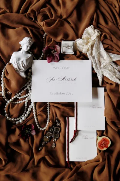Wedding stationery flat lay with invitation suite styling, anchored by an engagement ring, on brown draped fabric with neutral tones.
