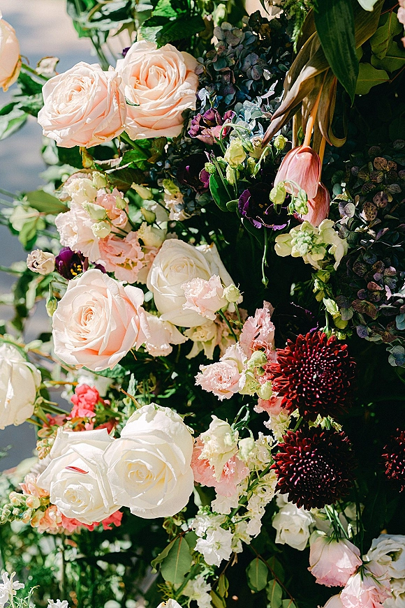Wedding floral arrangement with ceremony floral installation of blush roses, hydrangea, tulips, and lush greenery in soft outdoor light