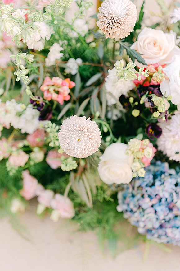 Wedding floral arrangement with roses and dahlias, soft blush and white blooms with greenery on a neutral surface with blurred florals behind