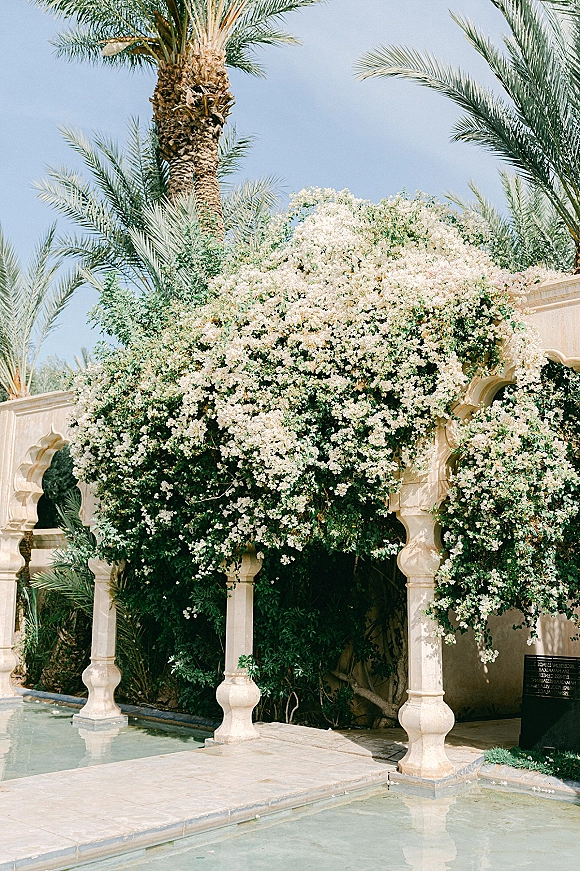 Outdoor wedding venue with garden wedding venue charm, stone arches draped in white blooms and greenery beside a reflecting pool in a palm courtyard