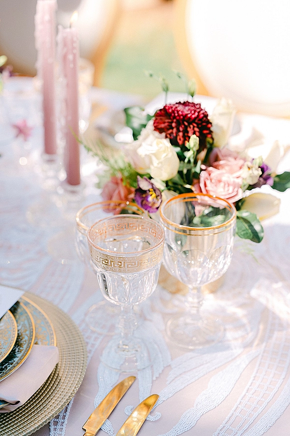Reception tablescape with wedding table setting, floral centerpiece, pink taper candles, and gold-rimmed goblets glowing in outdoor bokeh light