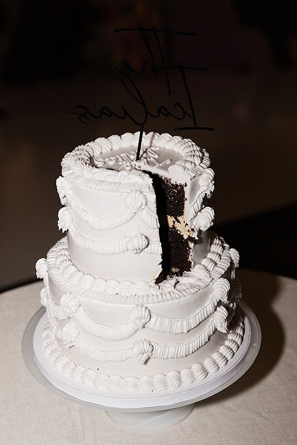Wedding cake with two tier wedding cake design, white frosting and piped buttercream garlands on a stand against a dark backdrop