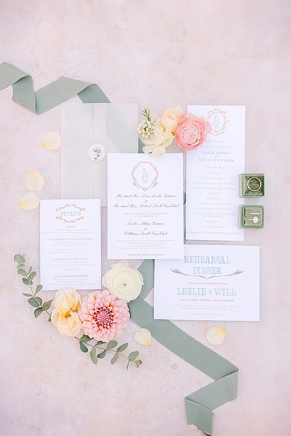 Invitation suite wedding invitation flat lay styled with silk ribbon, wax seal, rose petals, eucalyptus sprigs, and rings on stone surface