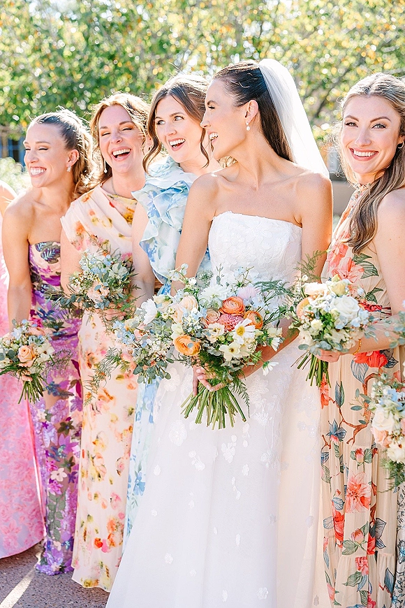 Bridesmaid group photo with bride and bridesmaids holding bouquets, bride in veil and strapless gown in a sunlit garden setting