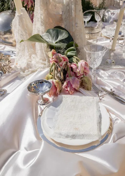 Wedding place setting featuring a lace napkin on plate, styled neatly on the table with a soft garden backdrop of lush plants