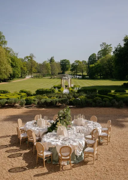 Reception tablescape for a garden wedding table, styled with taper candles and set on a garden lawn beside hedges and a tranquil pond.