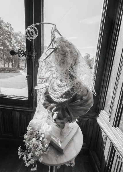 Bridal accessories styled with a lace wedding veil draped by a window framing garden trees and sky.