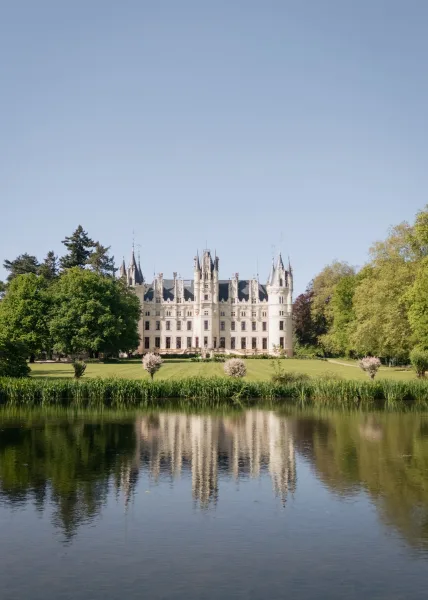 Castle wedding venue exuding chateau wedding venue elegance, its turrets mirrored in a tranquil lake beside a grand lawn and garden trees.