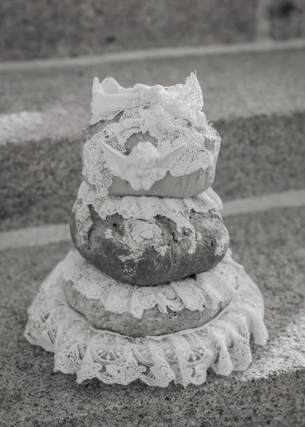 Bread wedding cake stacked from loaves as a savory wedding cake, crowned with a single cherub ornament and set on worn stone steps.