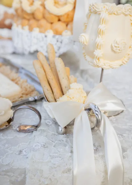 Wedding dessert table styled as an elegant sweets table, set on a lace tablecloth with a pastry tower and gleaming silver serveware.