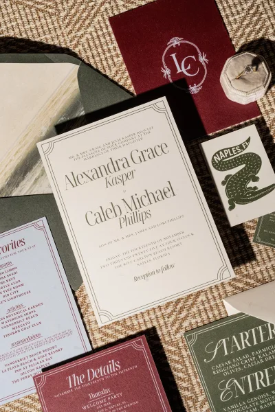 Invitation suite flat lay with wedding invitation card, RSVP and details cards, envelope, wax seal, and engagement ring on textured fabric surface