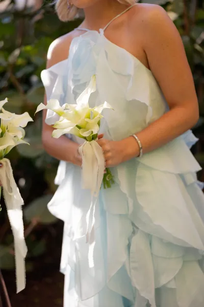 Bridesmaid portrait in a light blue bridesmaid dress holding a white calla lily bouquet with ribbon wrap against lush garden foliage