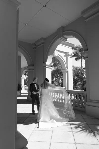 Wedding first look as groom sees bride in a strapless dress and cathedral veil, holding hands under an arched colonnade terrace