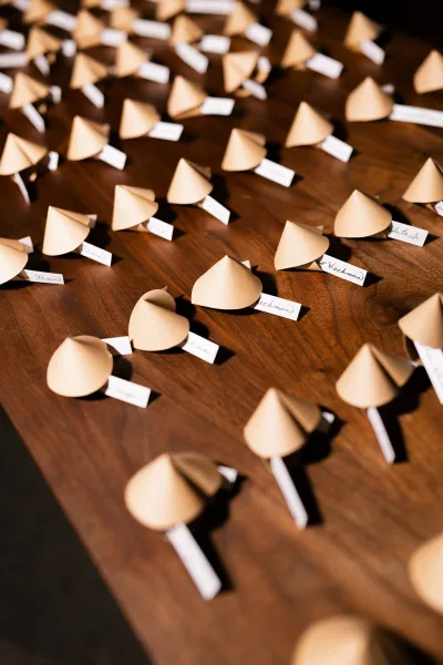 Wedding place cards arranged as an escort cards display with handwritten name tags in paper cone holders on a rustic wood table