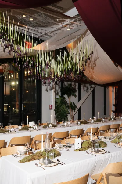 Reception tablescape with a long wedding table setup, moss runner and taper candles, set with glassware beneath draped ceiling and hanging calla lilies