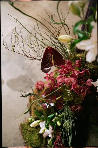 Wedding floral arrangement with ceremony floral installation styling, red anthurium and orchids over moss and greenery on a concrete floor