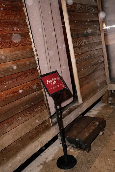 Wedding signage welcome wedding sign framed on a stand by a doorway with wood siding and steps as snow falls at the entrance