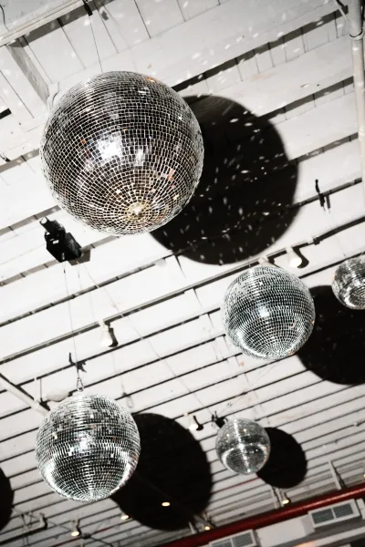 Disco ball decor with wedding disco balls hanging from cables and track lights, sparkling beneath an industrial white ceiling with beams