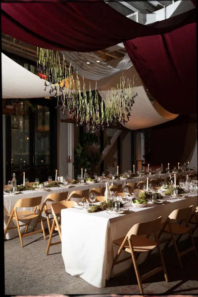 Reception tablescape on a long banquet table wedding with taper candles and greenery runner under draped fabric ceiling in an industrial venue