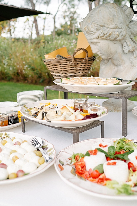Wedding grazing table with a wedding cheese platter of grapes, mozzarella, salads, and jam jars on tiered stands under a garden canopy