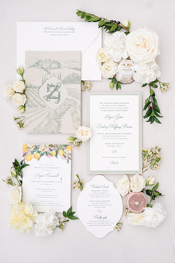 Invitation suite wedding invitation flat lay with letterpress cards, monogram crest, rings in a box, and white blooms on a neutral surface