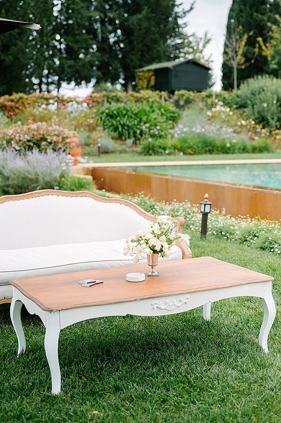 Lounge seating area outdoor wedding lounge with a vintage sofa and wood coffee table, floral centerpiece and lantern lights on a poolside lawn