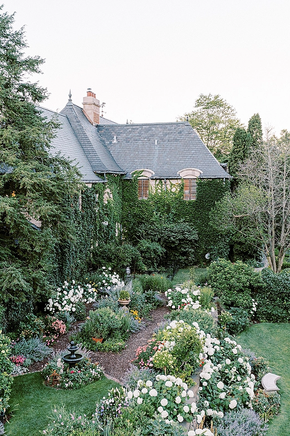 Wedding venue garden with white hydrangeas lining a garden path toward a small fountain beside ivy-covered walls and stone house