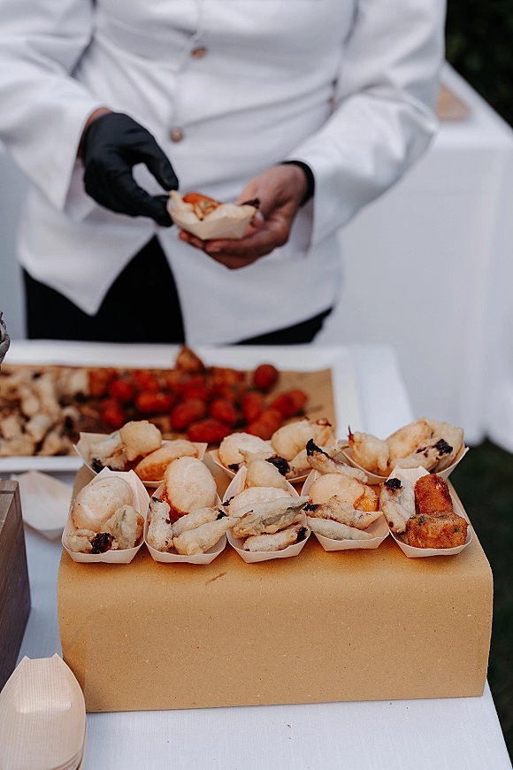 Wedding catering with a chef in a white coat and black glove passing fried cocktail hour appetizers in mini boats on a tray outdoors