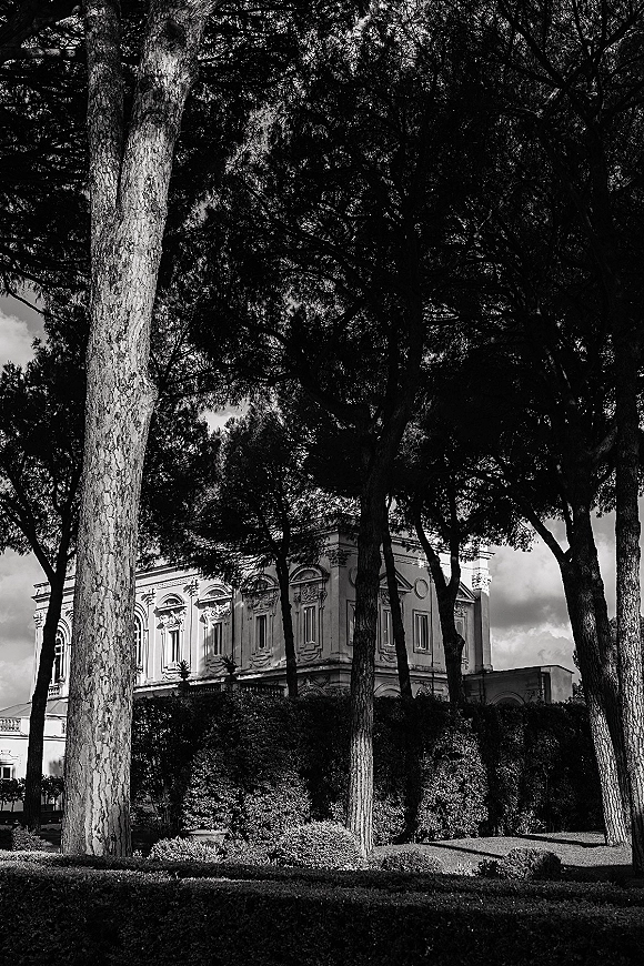 Wedding venue exterior of a grand estate wedding venue with historic facade, manicured hedges and lawn, framed by tall trees under cloudy sky