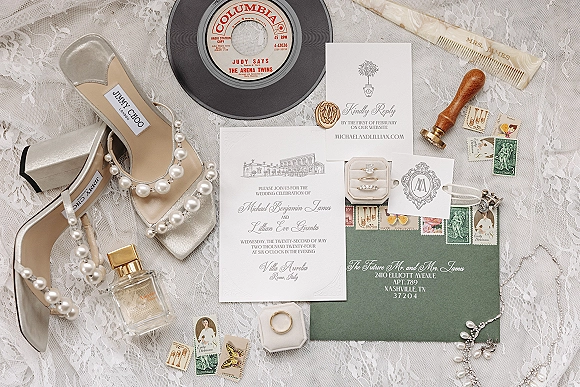 Invitation suite wedding invitation flat lay on lace fabric with envelope, RSVP and monogram cards, wax seal, stamps, rings, pearls and perfume
