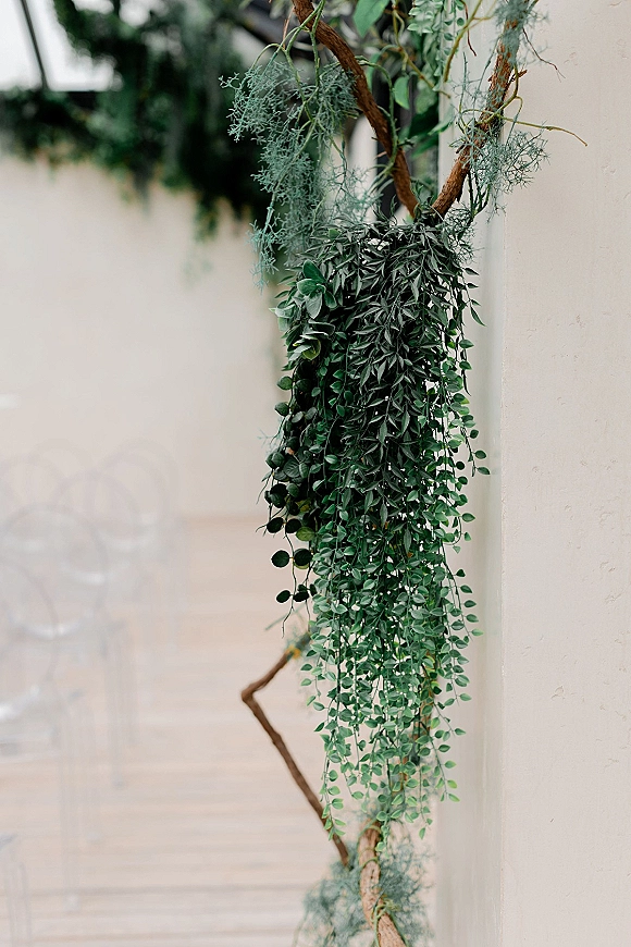 Wedding greenery decor with hanging greenery and eucalyptus vines draped over branches against a white wall along an outdoor walkway