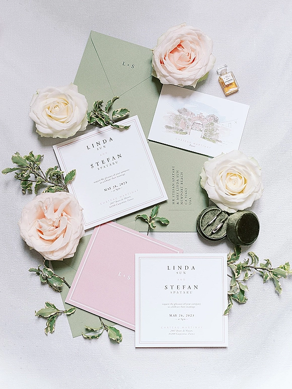 Invitation suite with sage green wedding invitations, RSVP card and envelopes with wax seal, roses and greenery on white fabric backdrop