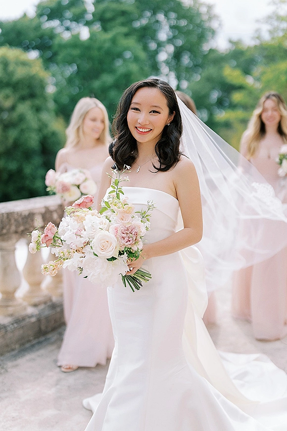 Bridal portrait of a bride holding bouquet in a strapless wedding dress with cathedral veil, on a garden terrace by stone balustrade