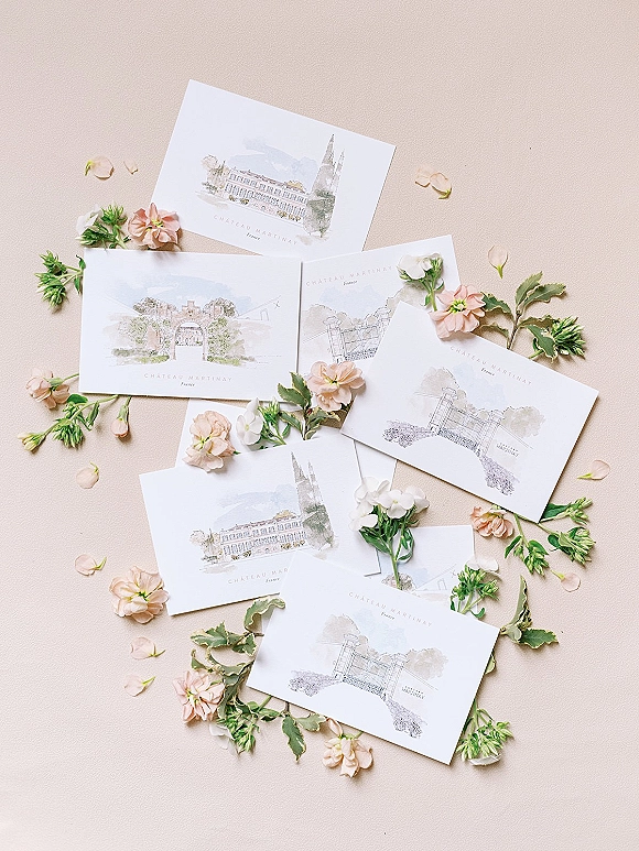 Invitation suite wedding invitation flat lay featuring watercolor venue illustrations with white envelopes and blush flowers on a beige paper backdrop