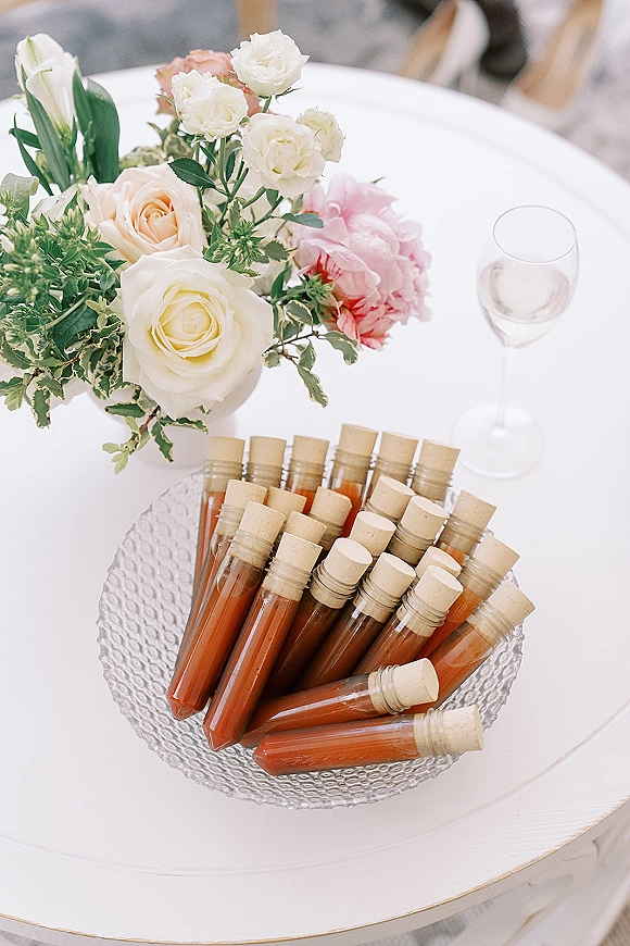 Wedding reception table with a wedding table centerpiece of white and peach roses in glass bowls, corked bottles, and a wine glass on a round white table