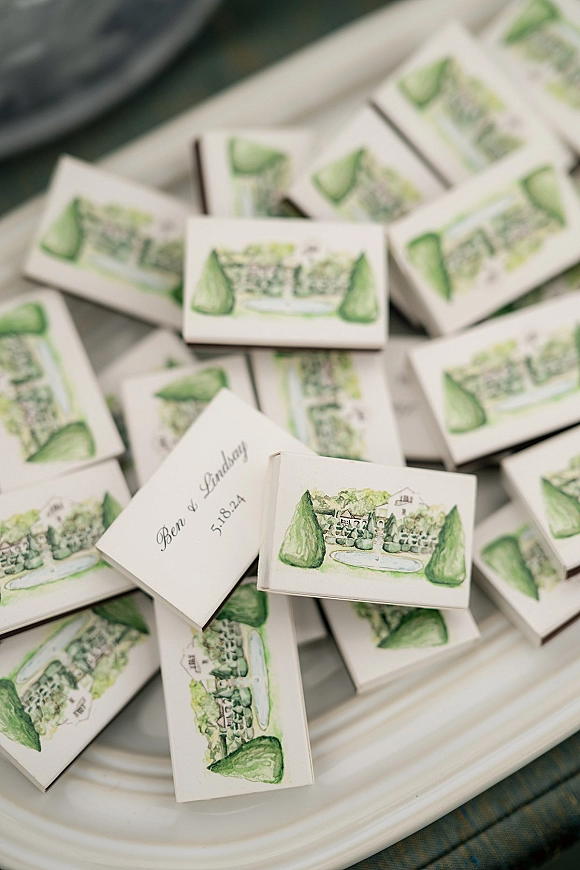 Wedding favors featuring personalized matchboxes with watercolor illustration, printed names and date, arranged on a white serving tray
