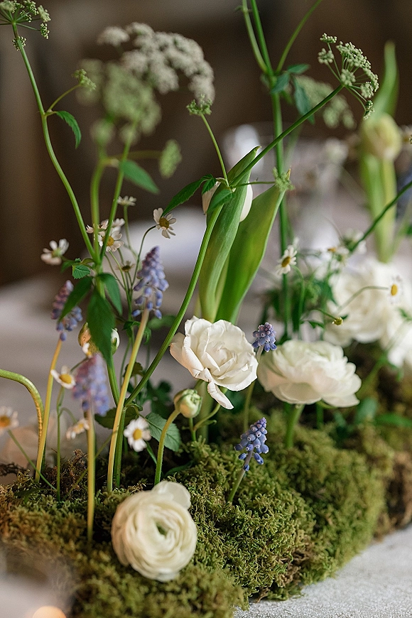 Floral centerpiece with ranunculus, lily buds, chamomile daisies and greenery in a ceramic bowl on a linen table at reception
