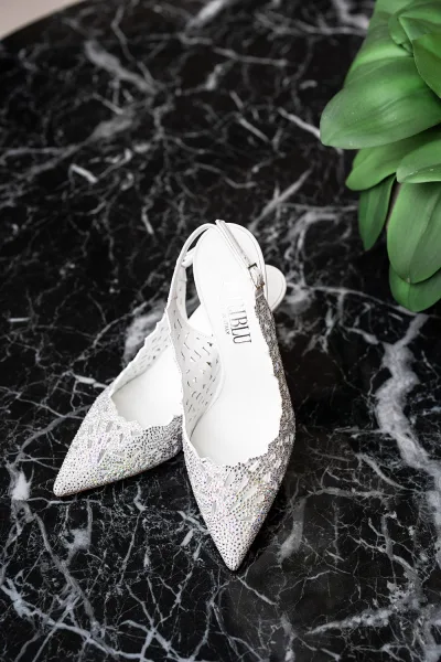 Bridal shoes with rhinestone detail and slingback straps, pointed toe perforated leather flats styled on black marble with green leaves