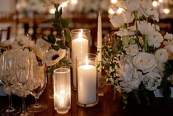 Reception tablescape with wedding table centerpiece of white roses, ranunculus and candles on wooden tables beneath bistro lights