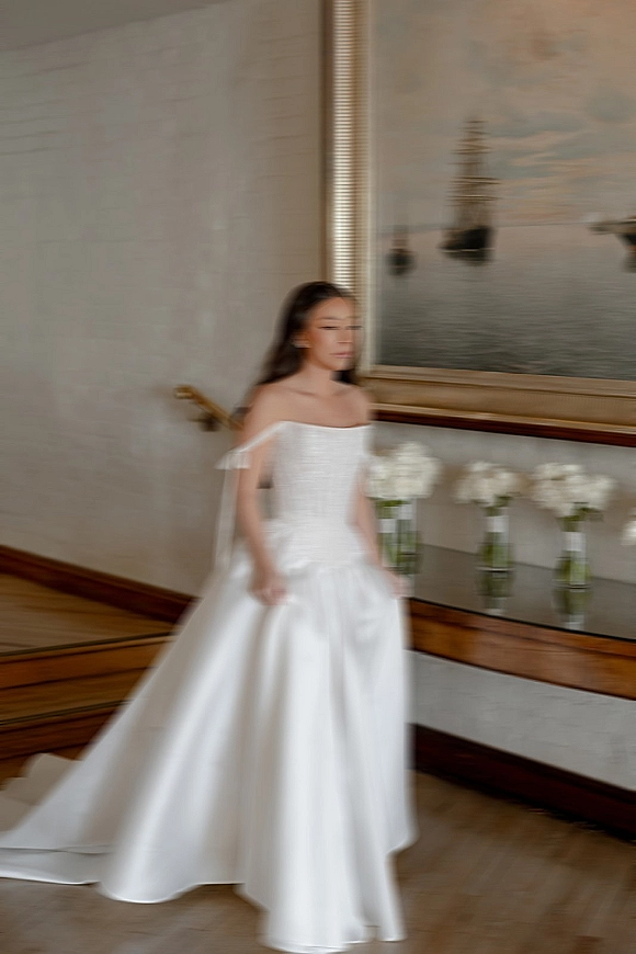 Bridal portrait of a bride in a strapless ballgown wedding dress with tulle sleeves and long train in a hotel hallway by white florals