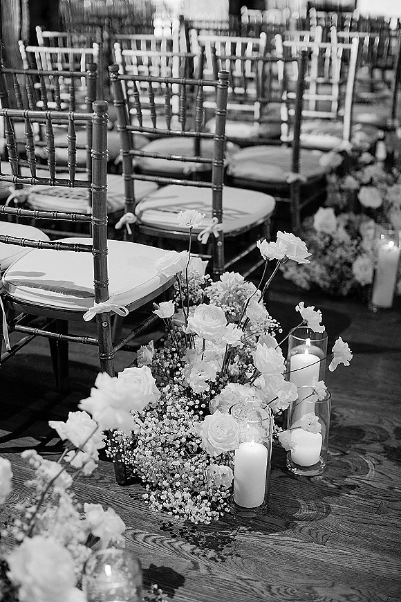 Ceremony aisle decor with wedding aisle flowers, roses and baby's breath beside pillar candles in glass vases on a wood floor aisle