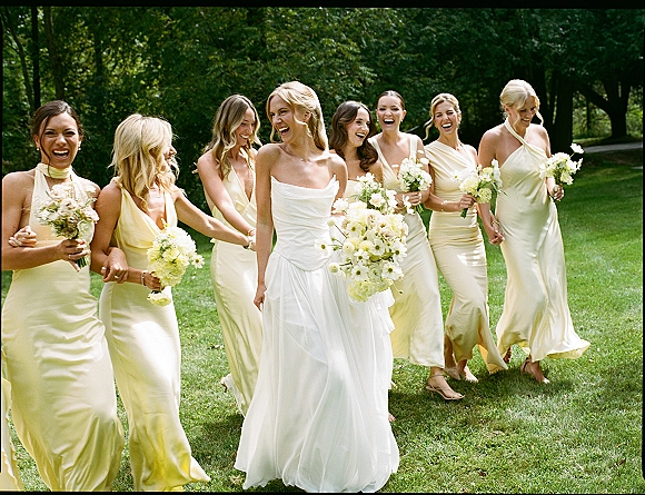 Bridesmaids with bride in pale yellow dresses, bridesmaid group photo as they laugh holding bouquets on a sunny park path
